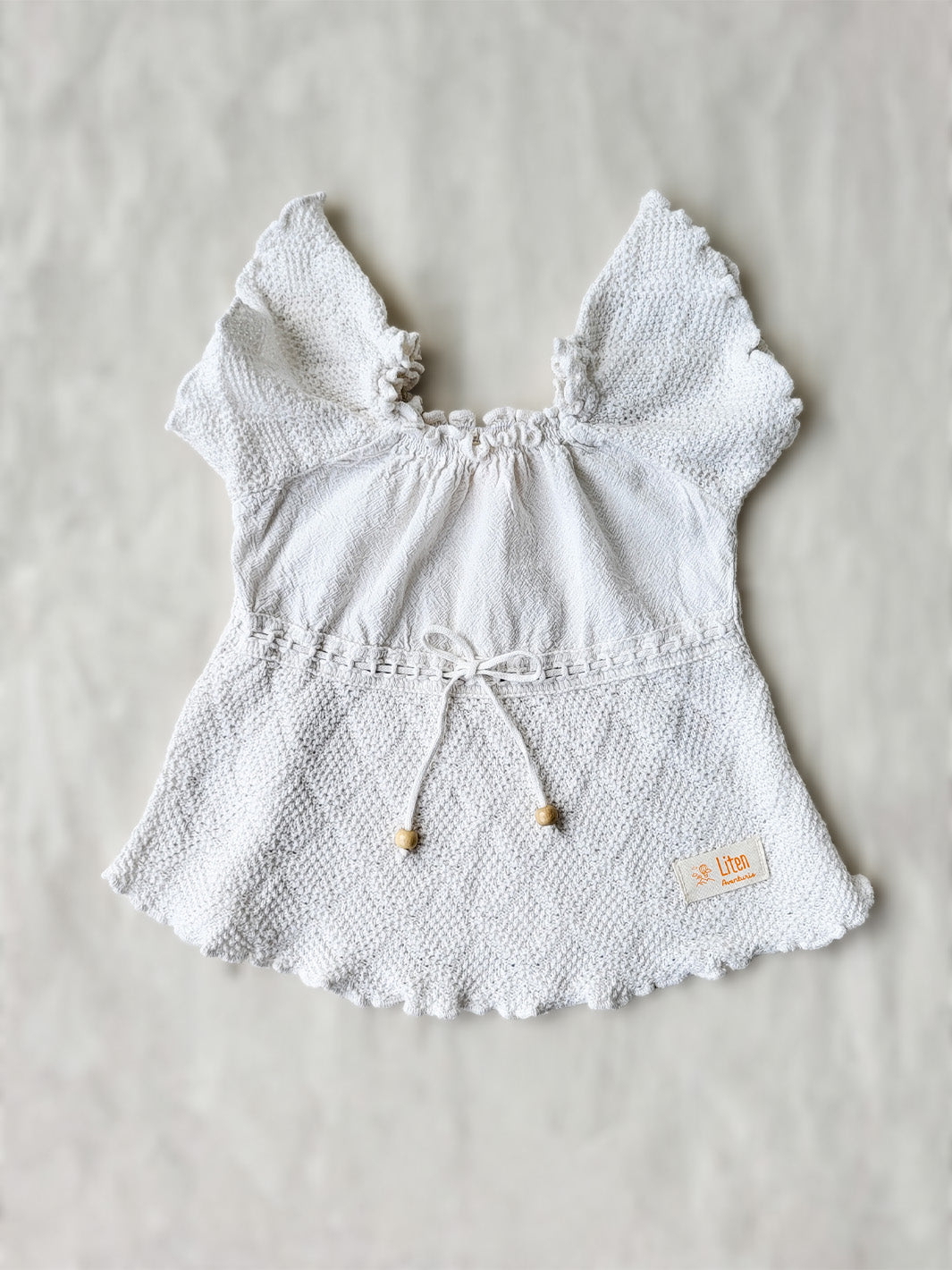 Liten Aventuris brand. Make a statement with the Annie Blouse! Crafted from soft cotton and featuring a playful knitted cotton pattern with drop-short sleeves. This blouse is perfect for any summer adventure. Prepare them for sunshine and comfort with fresh style. Perfect for girls. Barnkläder, Bomullskläder, Natural kläder. Flicka kläder. Flickblus. Barnblus.