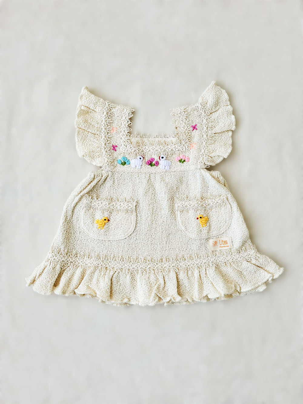 Liten Aventuris Collections. Experience the beauty of nature in the Elvita Dress! Hand-embroidered animals, flowers, and knitted cotton lace come together to create a whimsical look your little girl will love. With a snug A-line fit and playful butterfly sleeves, this dress is perfect for every outdoor adventure she can come up with. Natureâs beauty is literally at her fingertips! Made of natural peruvian knitted cotton, Ethically made in Peru. Ekologisk klänning fĂśr flickor och bebisar.
