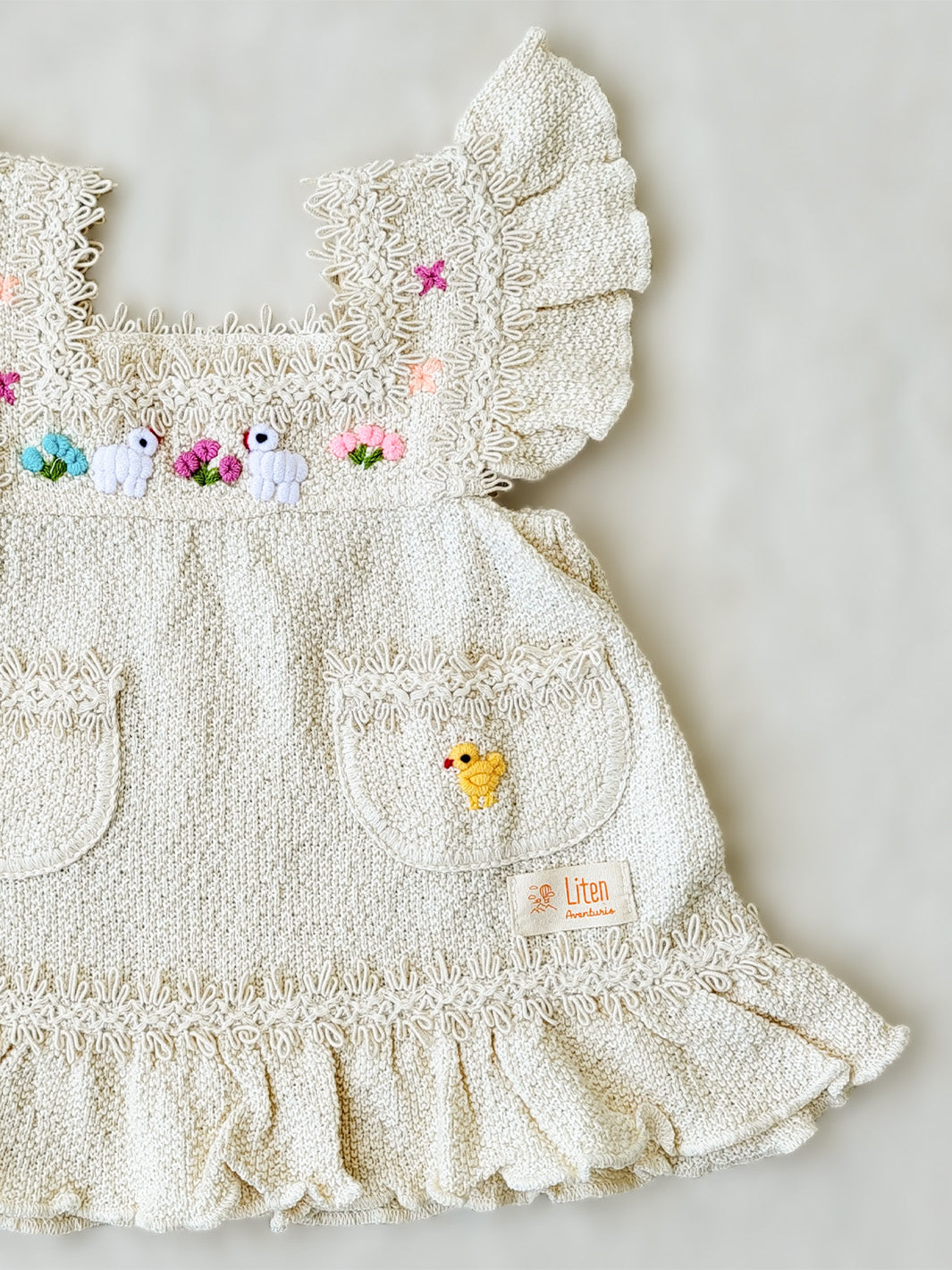 Liten Aventuris Collections. Experience the beauty of nature in the Elvita Dress! Hand-embroidered animals, flowers, and knitted cotton lace come together to create a whimsical look your little girl will love. With a snug A-line fit and playful butterfly sleeves, this dress is perfect for every outdoor adventure she can come up with. Natureâs beauty is literally at her fingertips! Made of natural peruvian knitted cotton, Ethically made in Peru. Ekologisk klänning fĂśr flickor och bebisar.