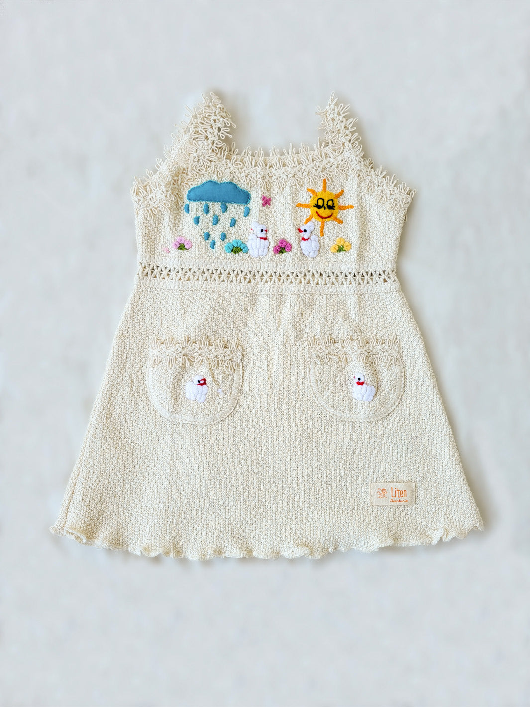 Liten Aventuris Collections. Dress your little star in this Estrella Dress! Featuring a strappy design, two front pockets with intricate cotton knitted lace, and colorful farm animal embroidery, your kiddo will be twinkling bright in no time! With its natural Peruvian Tanguis Cotton and star-inspired name, this dress will make your kids feel like they have the universe in their pocket! Ethically made in Peru. Ekologisk klänning fÜr flickor och bebisar.