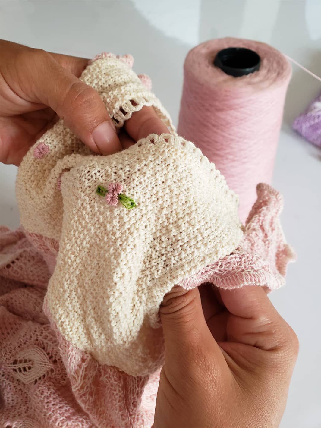 Hand embroidering a delicate flower on a knitted Tanguis cotton dress by Liten Aventuris, highlighting our artisanal work. | Handbrodering av en delikat blomma pü en stickad Tanguis-bomullklänning frün Liten Aventuris, som framhäver hantverksmässigan. | Bordado a mano de una delicada flor en un vestido de algodón Tanguis tejido de Liten Aventuris, resaltando lo artesanal.