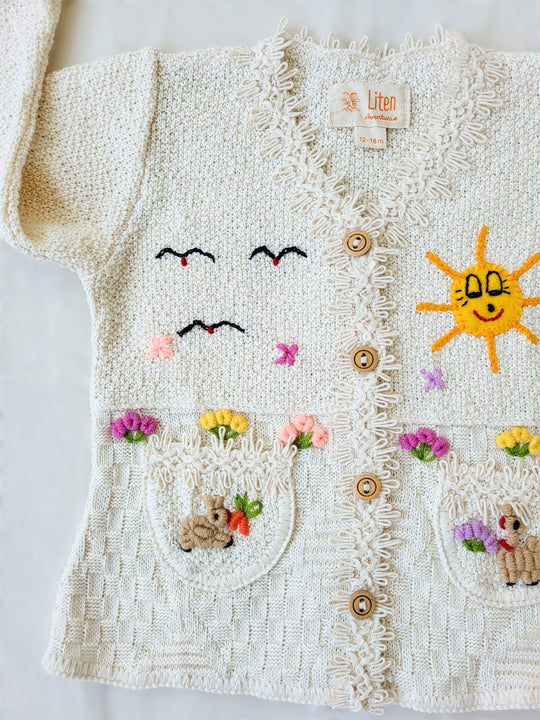 This Sandy Jacket is perfect for your little one's outdoor adventures! Our loose-fit jacket has hand-embroidered farm animals, flowers, and other nature-inspired design elements to give your stylish kid an extra-special look. Plus, two front pockets, and wooden buttons just for fun. Crafted with a combination of regular and geometrical knitted patterns. Liten Aventuris collections. Handbroderade barnkläder, Bomullsjacka, Barnjacka, Babyjacka.
