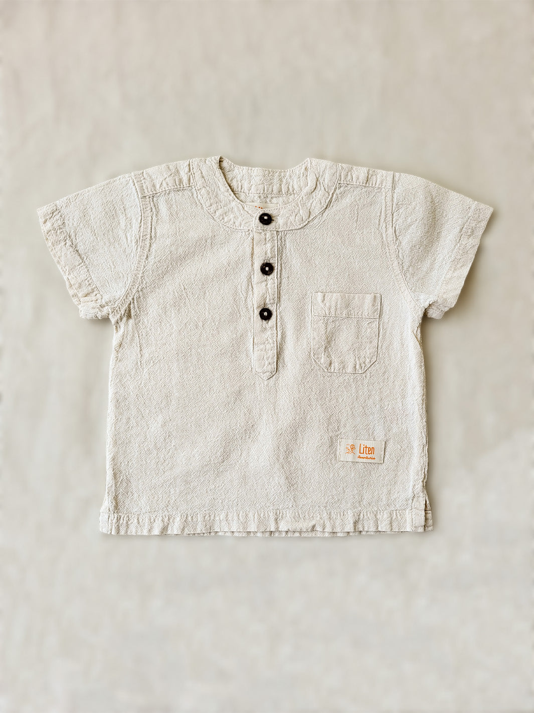 Liten Aventuris Natural Tocuyo Cotton shirt for kids. The Philipo shirt is perfect for a picnic at a lake or a nice morning stroll! This short sleeve shirt with coconut buttons and tunisian collar is casual and chic at the same time. This loose-fitting shirt with one pocket, is comfortable and soft with the skin. Ethically made in Peru. Bomullskläder, barnkläder, Pojken tröja, Natural kläder, ekologisk kläder.