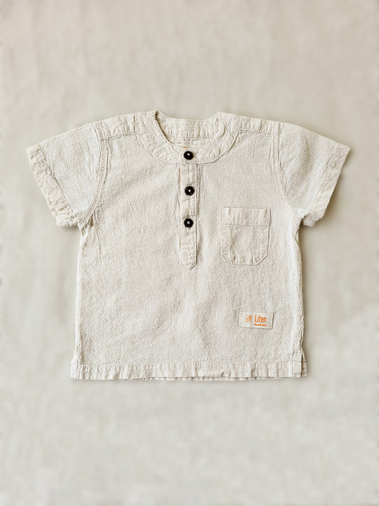 Liten Aventuris Natural Tocuyo Cotton shirt for kids. The Philipo shirt is perfect for a picnic at a lake or a nice morning stroll! This short sleeve shirt with coconut buttons and tunisian collar is casual and chic at the same time. This loose-fitting shirt with one pocket, is comfortable and soft with the skin. Ethically made in Peru. Bomullskläder, barnkläder, Pojken tröja, Natural kläder, ekologisk kläder.