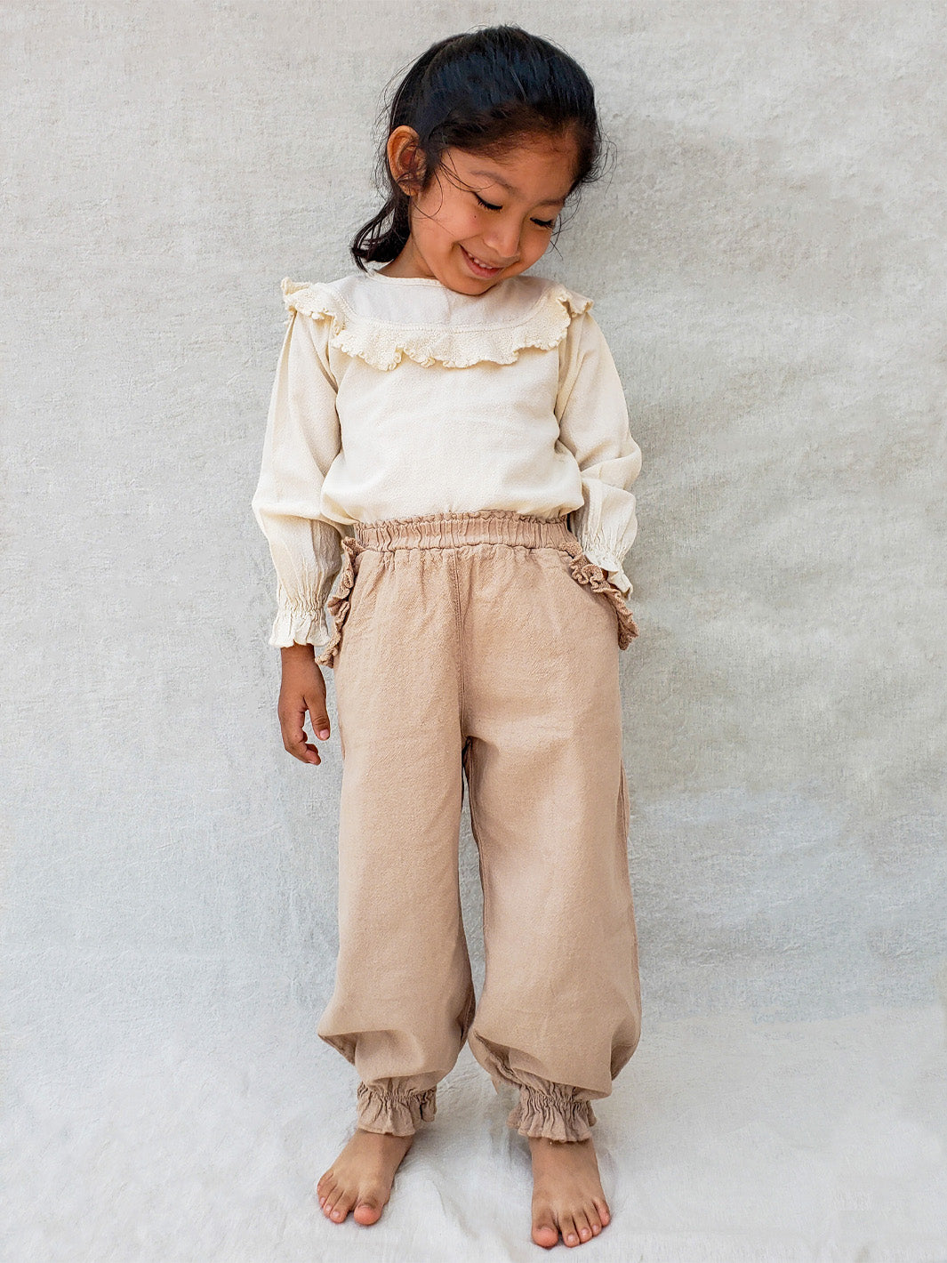 Liten Aventuris. Our Siri Blouse is elegant and comfortable at the same time. Its long sleeves with ruffles on the wrists are perfect for an evening stroll. The knitted cotton ruffles on the chest add a nice artisanal touch. Part of our Collection. Loose-fitting garment. 100% Flat-knitted Natural Peruvian Tocuyo Cotton. 100% knitted Natural Tanguis Cotton. Ethically made in Peru. Perfect for girls. Barnkläder, Bomullskläder, Natural kläder. Flicka kläder. Flickblus. Barnblus.