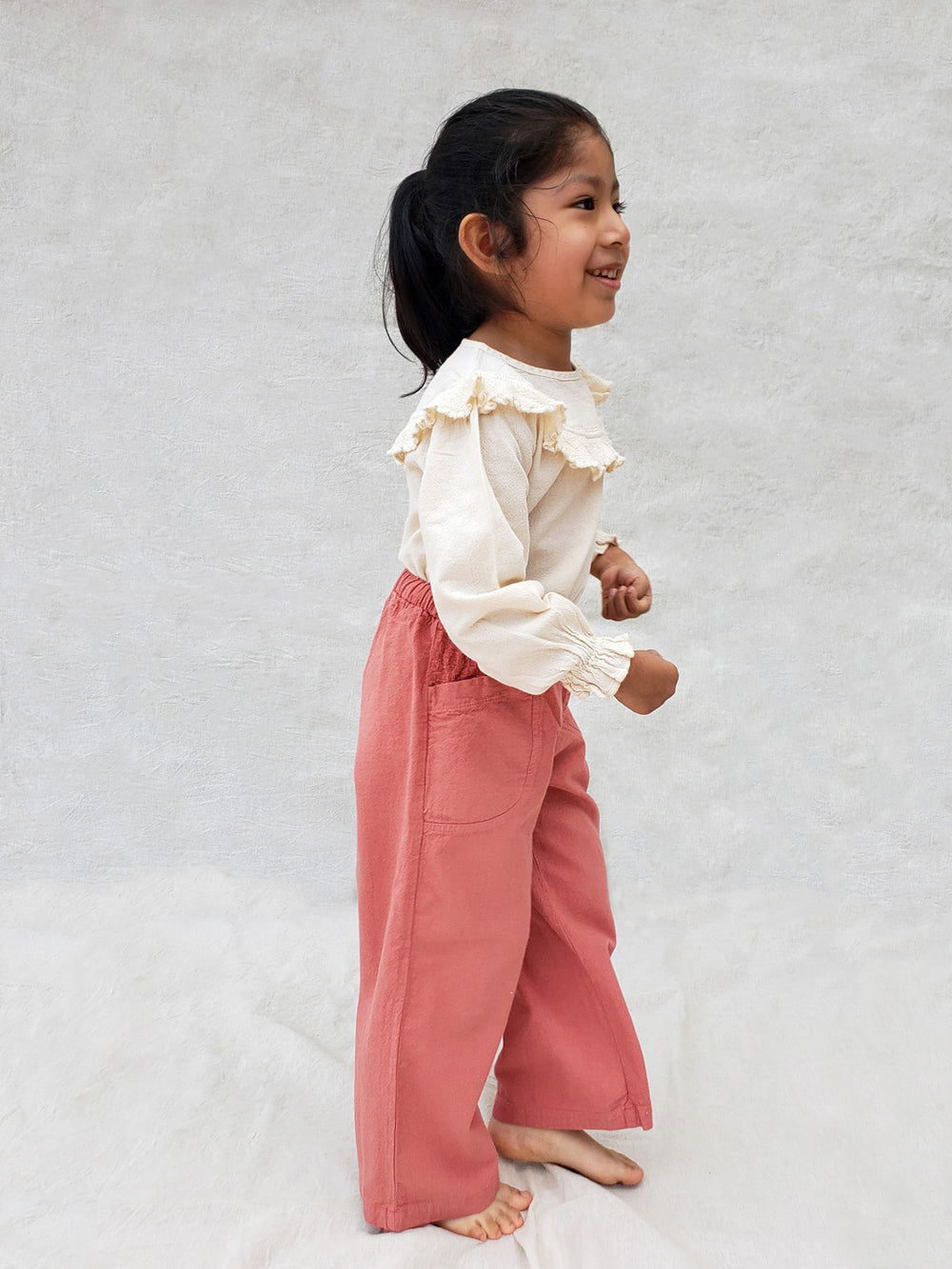 Liten Aventuris. Our Siri Blouse is elegant and comfortable at the same time. Its long sleeves with ruffles on the wrists are perfect for an evening stroll. The knitted cotton ruffles on the chest add a nice artisanal touch. Part of our Collection. Loose-fitting garment. 100% Flat-knitted Natural Peruvian Tocuyo Cotton. 100% knitted Natural Tanguis Cotton. Ethically made in Peru. Perfect for girls. Barnkläder, Bomullskläder, Natural kläder. Flicka kläder. Flickblus. Barnblus.