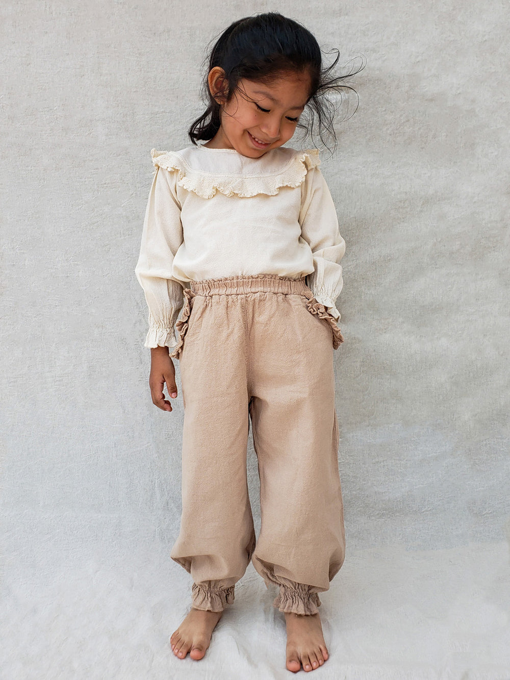 The Siri Pants are elegant and comfortable at the same time. These bloomer pants with ruffles at the bottom are perfect for a walk on the beach or a nice play date at the park. The Siri Pants bring two pockets with knitted cotton ruffles on them. It adds a nice artisanal touch. Beautiful, chic, and charming!  Make the perfect match with the Siri blouse. 100% Natural Peruvian Tocuyo Cotton. Perfect for girls. Barnkläder, Bomullskläder, Natural kläder. Flicka kläder. Barn Byxor.