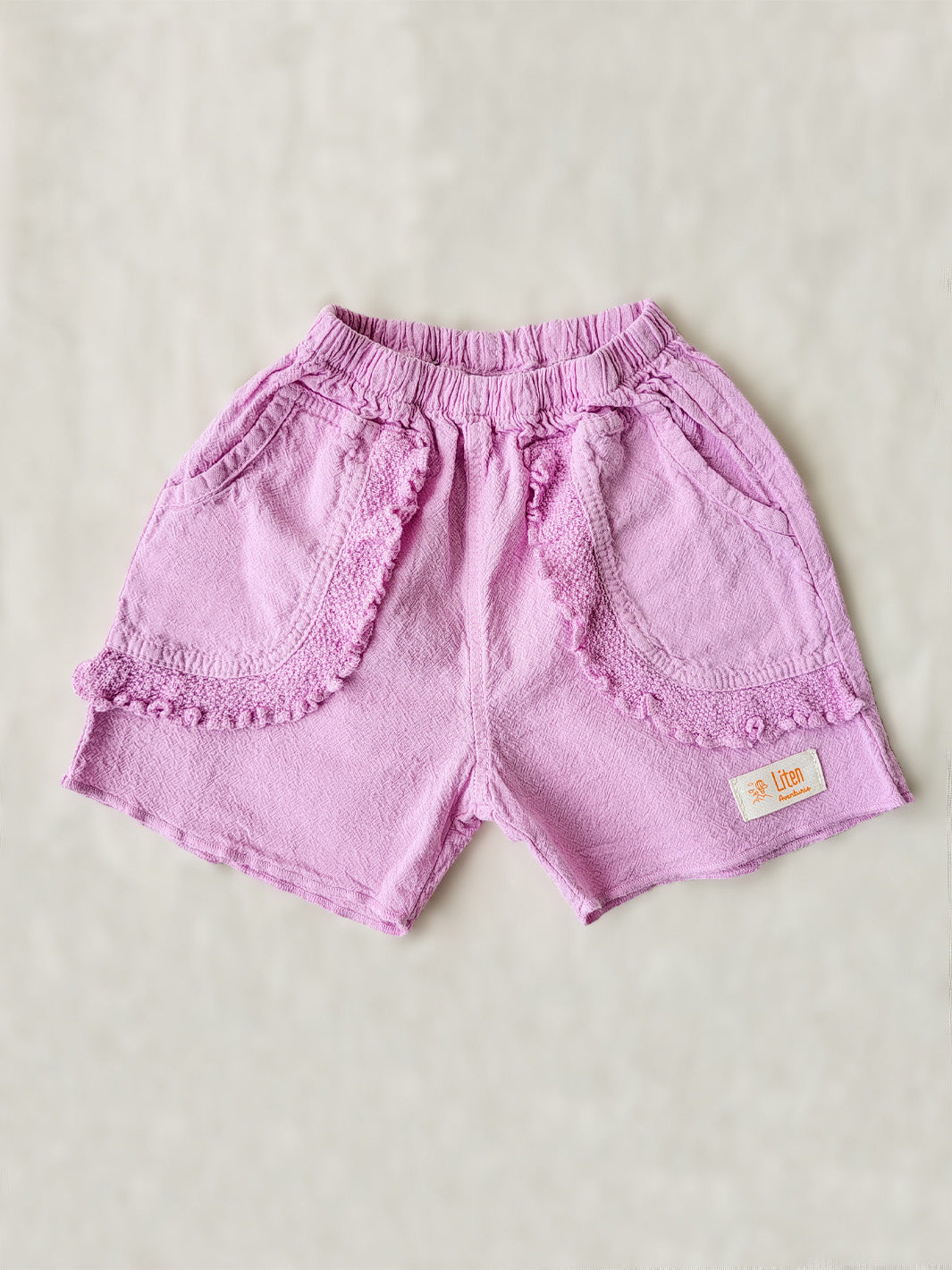Take her on an adventure in style with these Liss Shorts! Made from natural cotton in a vibrant Malva pink color, they're the perfect combo of cute and comfy. And of course, those front pockets with knitted cotton ruffles - because no outfit is complete without a little something extra! Pair the Liss Shorts with any top from our Liten Aventuris collections and your little one will be ready to take on any challenge! Flickan kortbyxor, barn bomullskläder.