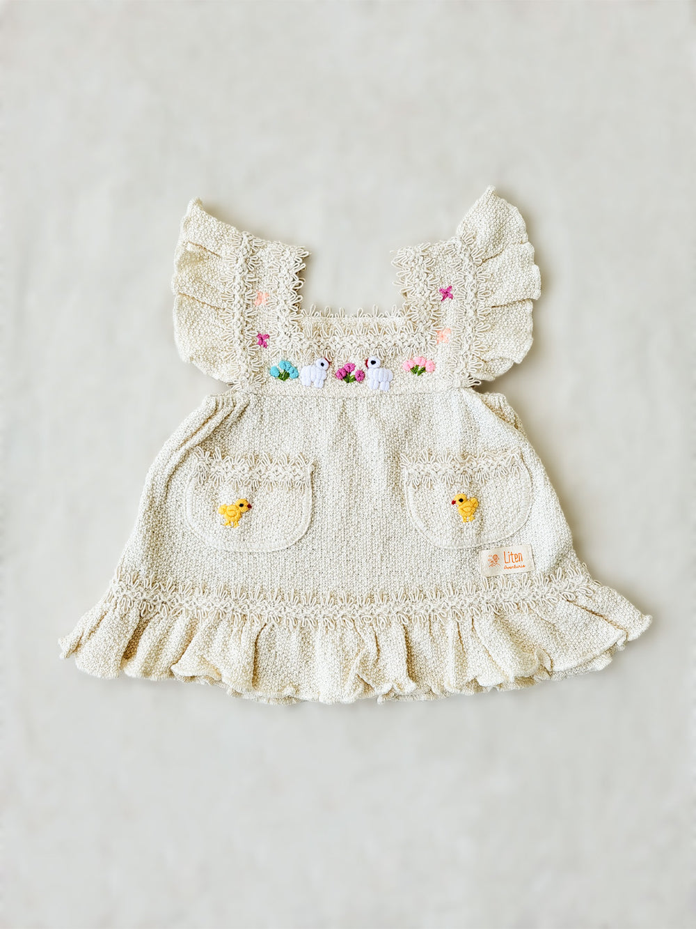 Liten Aventuris Collections. Experience the beauty of nature in the Elvita Dress! Hand-embroidered animals, flowers, and knitted cotton lace come together to create a whimsical look your little girl will love. With a snug A-line fit and playful butterfly sleeves, this dress is perfect for every outdoor adventure she can come up with. Nature’s beauty is literally at her fingertips! Made of natural peruvian knitted cotton, Ethically made in Peru. Ekologisk klänning för flickor och bebisar.