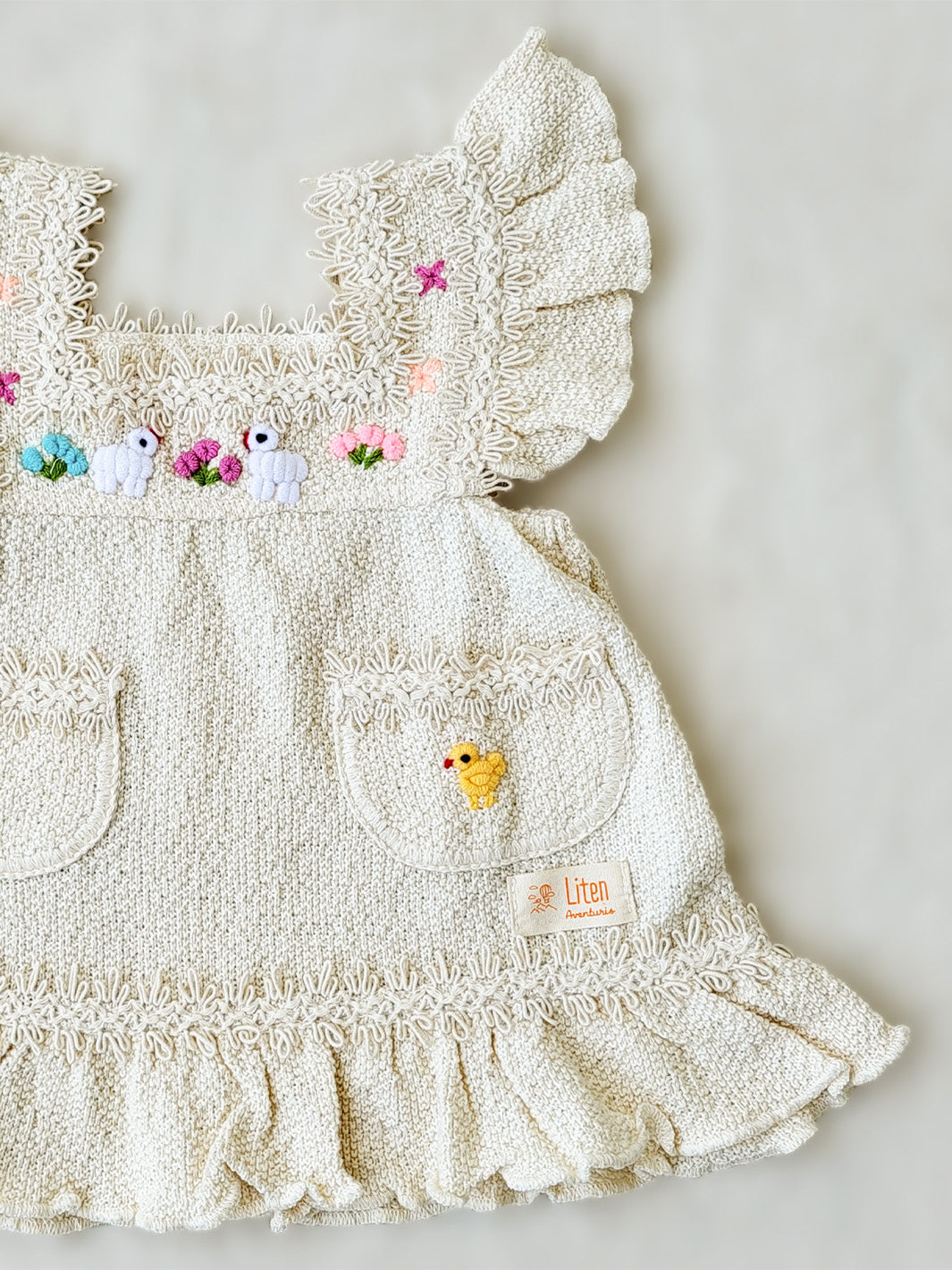 Liten Aventuris Collections. Experience the beauty of nature in the Elvita Dress! Hand-embroidered animals, flowers, and knitted cotton lace come together to create a whimsical look your little girl will love. With a snug A-line fit and playful butterfly sleeves, this dress is perfect for every outdoor adventure she can come up with. Nature’s beauty is literally at her fingertips! Made of natural peruvian knitted cotton, Ethically made in Peru. Ekologisk klänning för flickor och bebisar.