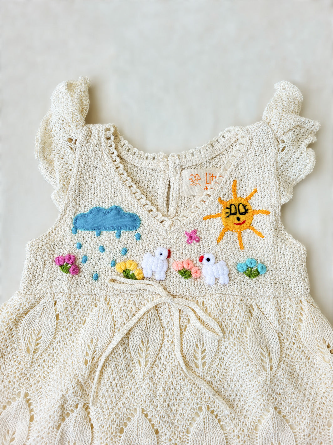 Explore the wild outdoors with your little one in the Pia Dress. Hand-embroidered with colorful designs inspired by farm animals and nature. Its cap sleeves and button behind the neck allow the perfect fit. This unique piece will spark your little one's imagination! A truly artisanal piece, with its natural cotton knitted pattern inspired by leaves and its inner layer in jersey cotton! Ekologisk klänning för flickor och bebisar.