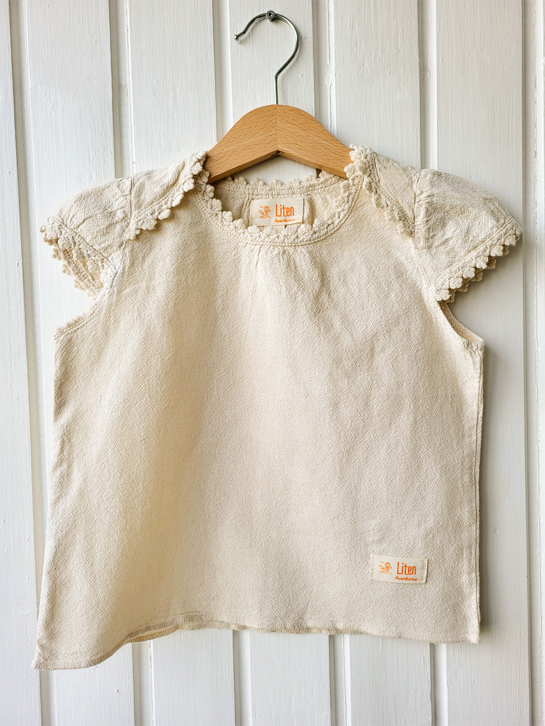 Liten Aventuris Natural Tocuyo Cotton blouse for kids. Our Lorin blouse is perfect for sunny days. With its loose-fitting shape and its embroidered detailed ribbon around the neck and sleeves, this blouse will be the best complement to any outfit! Perfect for girls. Barnkläder, Bomullskläder, Natural kläder. Flicka kläder. Flickblus. Barnblus.