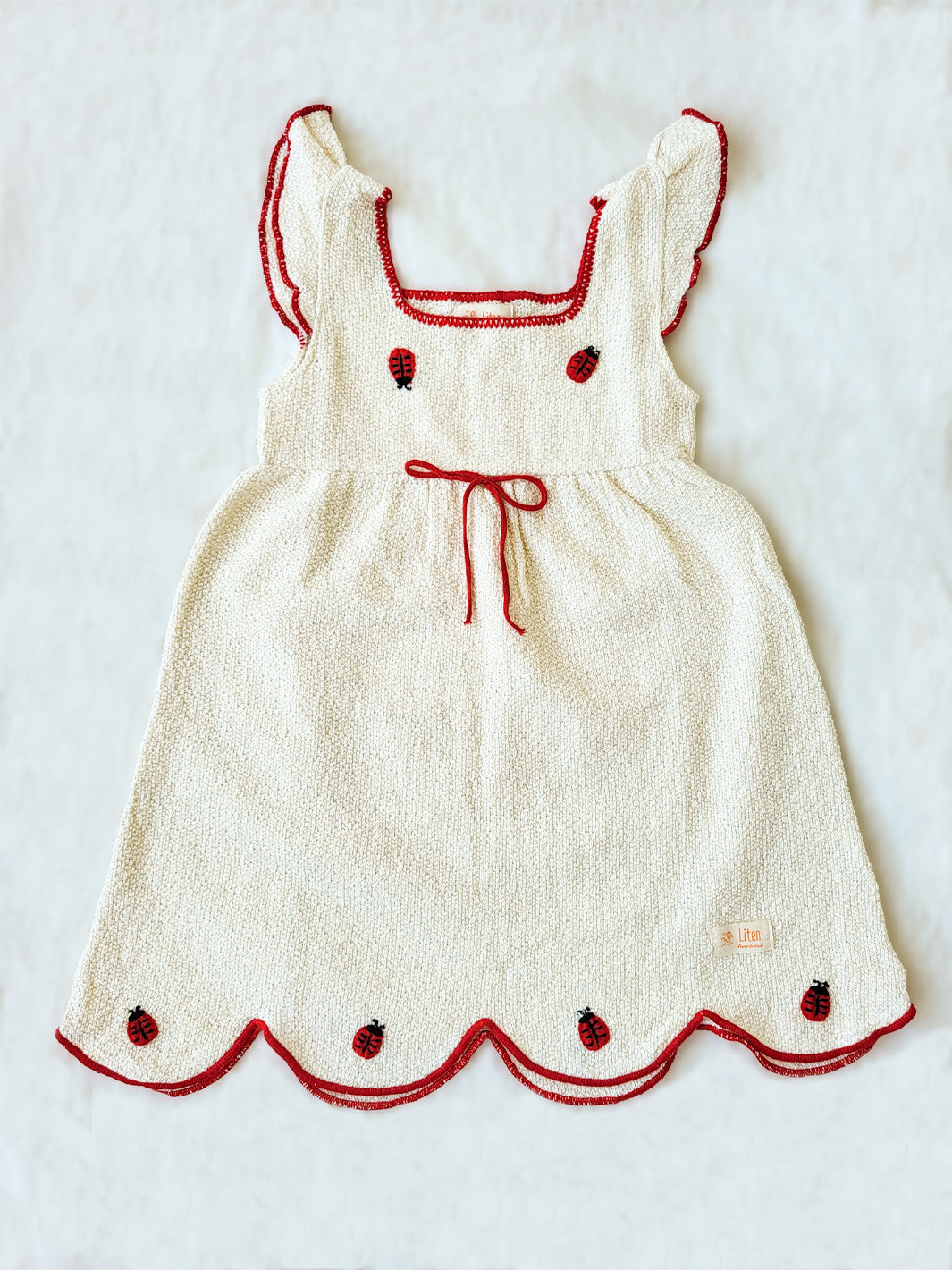 Liten Aventuris Collections. Bring luck and charm to your little one with this Zafirina dress! There's the belief in Italy that a ladybug brings good luck to the person it lands on. And we wanted to bring some luck to your little one. A knitted dress from Peruvian Cotton, and red knitted finishes bring a pop of color to this sweet garment. Hand-embroidered ladybugs playfully perch around the wavy-cut skirt, it's easy to see why Italy believes in good luck! Bomullsklänning för babis och flickor.